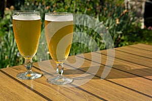 Two cold light unfiltered beer in glasses served on sunny outdoor terrace in garden