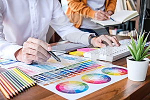 Two colleague creative graphic designer working on color selection and color swatches, drawing on graphics tablet at workplace