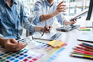 Two colleague creative graphic designer working on color selection and color swatches, drawing on graphics tablet at workplace