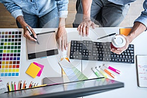 Two colleague creative graphic designer working on color selection and color swatches, drawing on graphics tablet at workplace