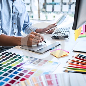 Two colleague creative graphic designer working on color selection and color swatches, drawing on graphics tablet at workplace