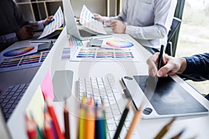 Two colleague creative graphic designer working on color selection and color swatches, drawing on graphics tablet at workplace wi