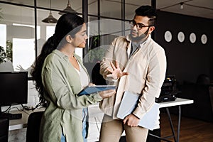 Two colleagues discussing business details while standing in modern office