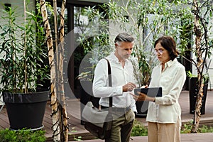 Two colleagues discussing business details and using tablet while standing outdoors