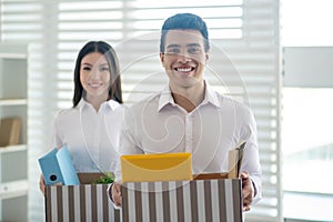 Two colleagues holding boxes with office stuff and smiling