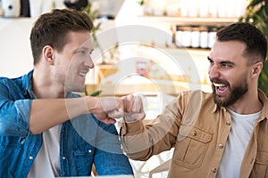 Two colleagues men bumping their fists looking happy and winning during lunch break at cafe, body language concept