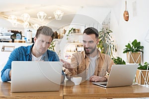 Two colleagues men discussing work issues during lunch break at cafe, working in their laptops, multitasking and teamwork concept