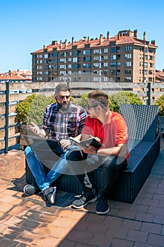 Two colleagues working with laptop sitting on office rooftop