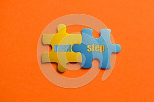 Two colored details of puzzle with text next step on orange background, Yellow and Blue, close up.