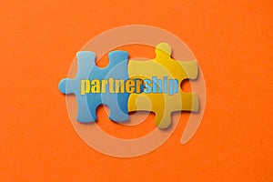 Two colored details of puzzle with text Partnership on orange background, Yellow and Blue, close up