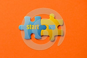 Two colored details of puzzle with text start up on orange background, Yellow and Blue, close up