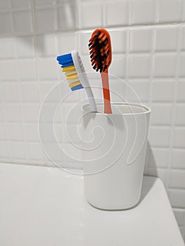 Two colored toothbrushes in white plastic glass.