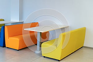 Two colorful armchairs sofas with a table in the room. Yellow and orange benchs. Interior design. School