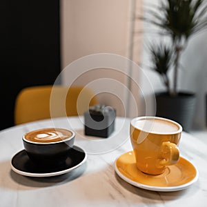 Two colorful ceramic coffee cups stand on a table in a vintage cafe with a delicious cappuccino and sweet latte. Good morning