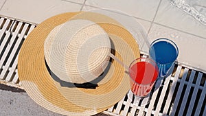 Two colorful cocktail glasses pink and blue, sun hat on the edge of the swimming pool, close up. Vacation concept, hotel