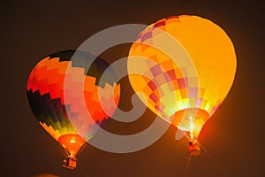 Two colorful hot air balloons flying with flames against dark sky