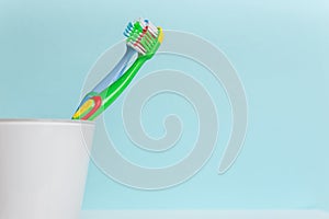 Two colorful kids toothbrushes in white cup on cyan  color background. Space for text.  Dental care concept
