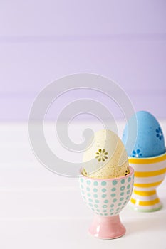 Two colorful painted Easter eggs in vibrant modern egg stands on pastel lilac background