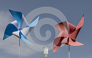 Two colorful paper pinwheels and a lit light bulb, make the concept of clean wind energy, against the blue sky