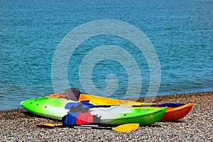 Two colorful sea kayaks with paddles and life jackets on stony beach