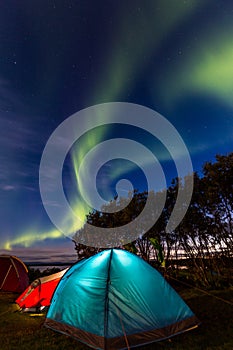 Two colorful sleeping tents under a night sky with green northern lights