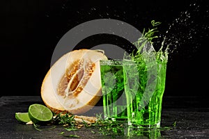 Two colorful splashing tarragon cocktails on a black background. Green tarragon, cut sweet melon, and sour lime.