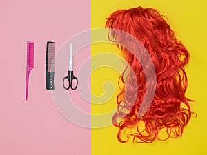 Two combs, scissors and a bright orange wig on a two-tone background. Accessories to create style.