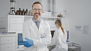 Two committed lab mates, a man and woman, standing relaxed with crossed arms in the heart of their science research workspace