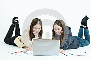 Two concerned young brunette twins sisters girls in vivid colorful clothes hold, using laptop pc computer isolated on