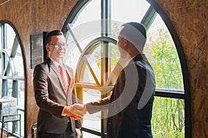 Two confident businessman shaking hands for demonstrating their agreement to sign agreement or contract between their firms