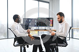 Two confident businessmen, financial analysts or investment advisers sitting at office desk