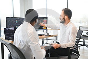 Two confident businessmen, financial analysts or investment advisers sitting at office desk