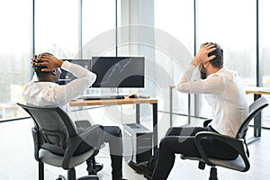 Two confident businessmen, financial analysts or investment advisers sitting at office desk