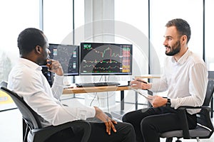 Two confident businessmen, financial analysts or investment advisers sitting at office desk