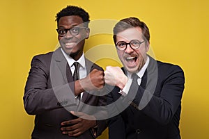 Two confident men in suit, african and caucasian guys making fist bumping