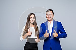 Two confident smiling businesspeople in formalwear showing thumbs-up on gray background