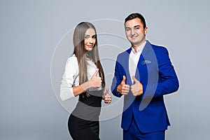 Two confident smiling businesspeople in formalwear showing thumbs-up on gray background