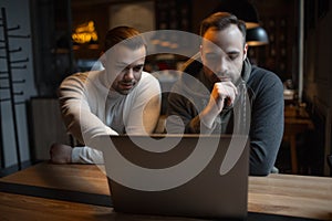 Two confident young businessmen working at laptop