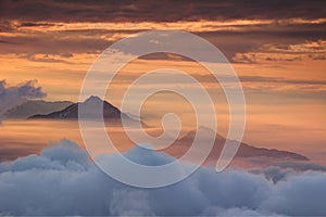 Two conical peaks above translucent autumn morning orange mist