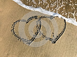 Two connected Hearts drawn on the beach sand with sea waves