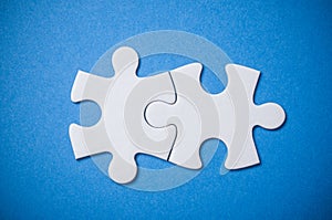 Two connected jigsaw puzzle pieces on blue background. The concept of finding the right solutions in teamwork