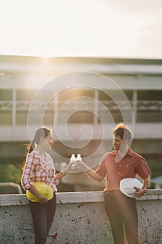 Two construction engineers celebrate after work or project at construction site or factory, man and woman bumping water bottles