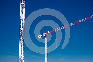 Two construction tower cranes at a construction site against a blue sky with clouds. Modern high-rise office building