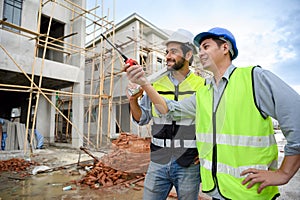 Two constructions man in vests with helmets working on under-construction building site. Engineer foreman discusses with a