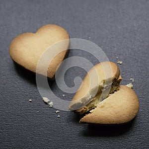 Two cookies in the shape of heart, one of them is broken on black background. Cracked heart shaped cookie as concept of breakup