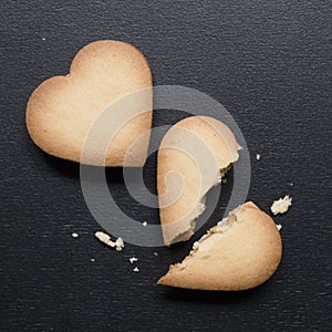 Two cookies in the shape of heart, one of them is broken on black background. Cracked heart shaped cookie as concept of breakup