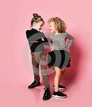 Two cool kids girls best friends sisters in leopard print clothes pants and sweatshirts are turned to look at each other