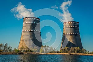 Two cooling towers of a nuclear power plant near a lake against a blue sky. Ecological energy production.