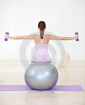 The two core components to her workout. Rearview shot of a young woman sitting on an exercise ball and doing some