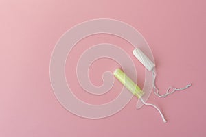 Two cotton tampons with light green applicator and without applicator on a pink background. Hygienic types of tampons.